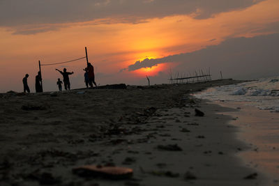 Silhouette people on beach against sky during sunset