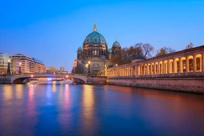 View of canal in city lit up at night against clear sky