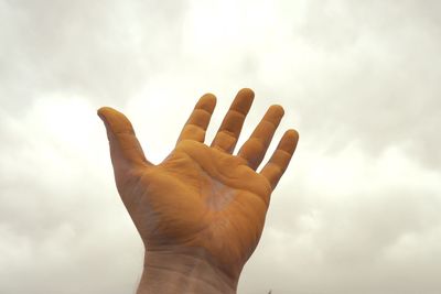 Low angle view of human hand with yellow paint against cloudy sky