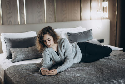 Young woman using mobile phone while lying on bed at home