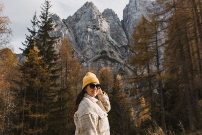Portrait of happy young woman standing under beautiful mountains in autumn