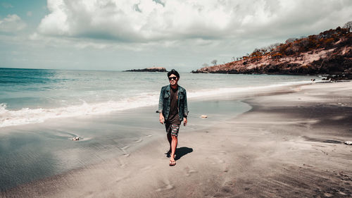 Full length of young man standing on beach against sky