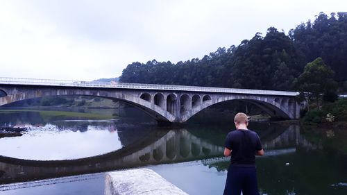 Rear view of boy standing against bridge at lake