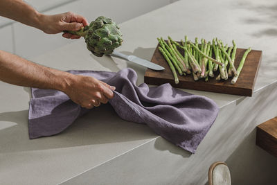 Cropped hand of person holding vegetables on table