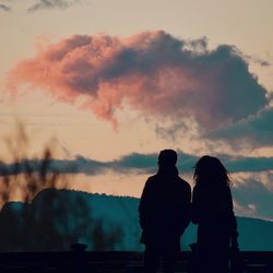 Rear view of silhouette couple standing against sky during sunset