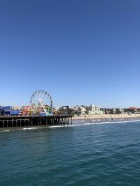 View of ferris wheel in city against clear blue sky