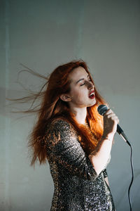 Portrait of redhead female singer woman in sparkly evening dress holding microphone