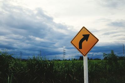 Road sign on field against cloudy sky