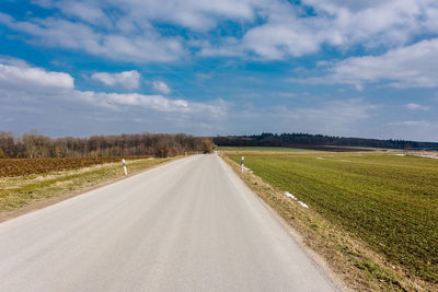 Empty road amidst field against sky