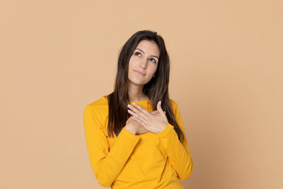 Portrait of young woman standing against yellow background