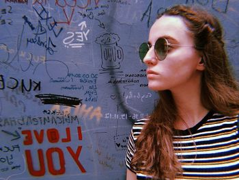 Young woman wearing sunglasses against graffiti wall