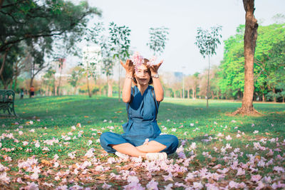 Portrait of woman throwing flowers on field at park