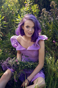 Teenage girl with dyed purple hair and a nose piercing in the grass with a bouquet of flowers