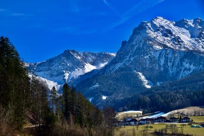 Scenic view of landscape with houses and snowcapped mountains against blue sky