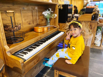 Beautiful girl in yellow dress sitting on the piano chair