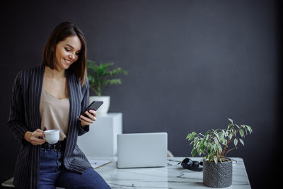 A young girl sits in the office on the table and uses a smartphone