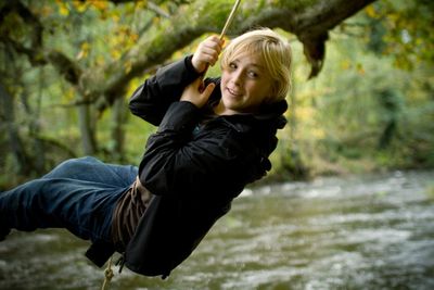 Young woman swinging on rope over river in forest