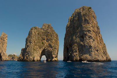 Rock formation in sea against clear blue sky