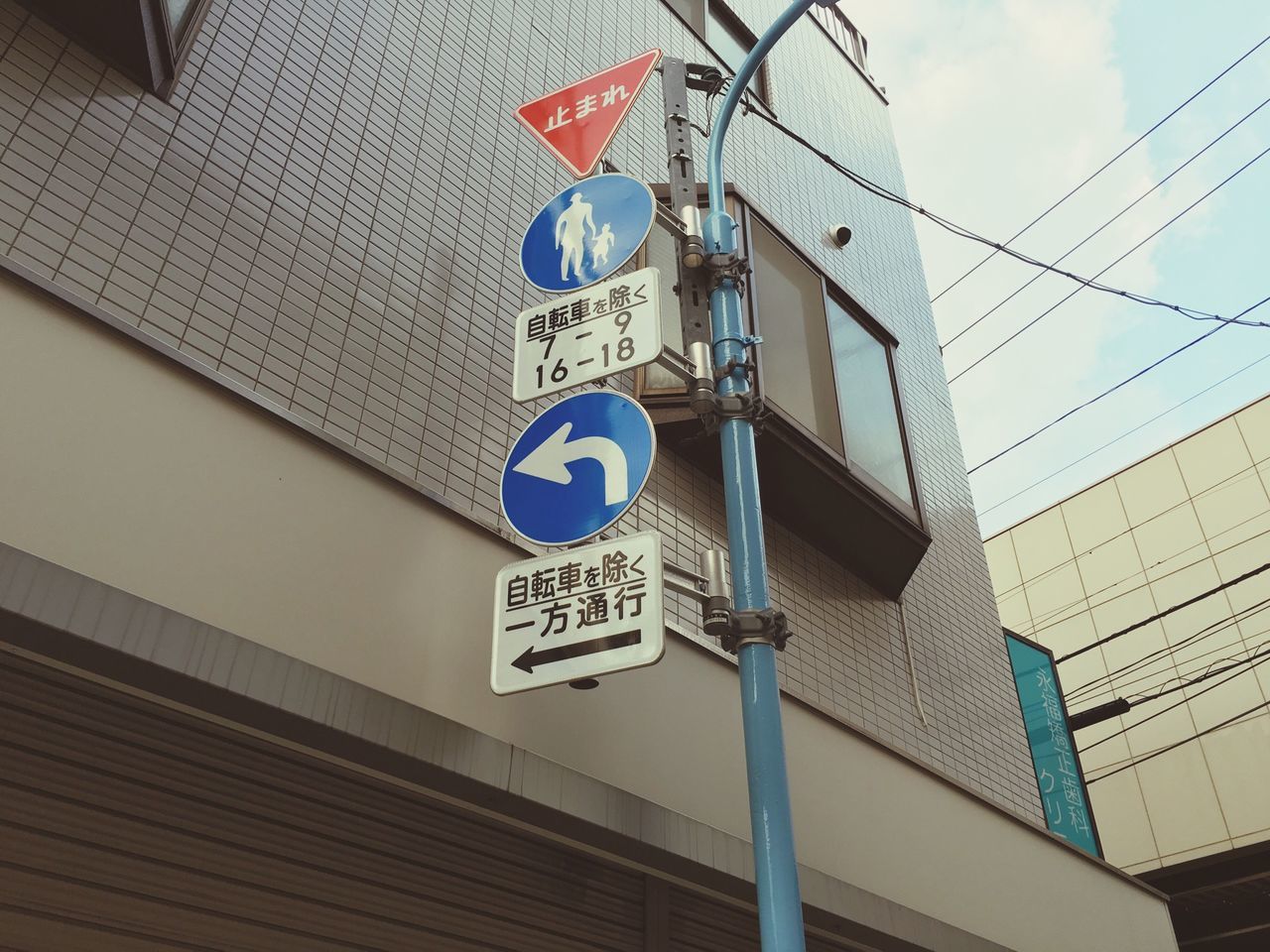 low angle view, architecture, text, built structure, building exterior, communication, western script, guidance, city, information sign, road sign, sign, building, sky, information, pole, non-western script, directional sign, capital letter, day