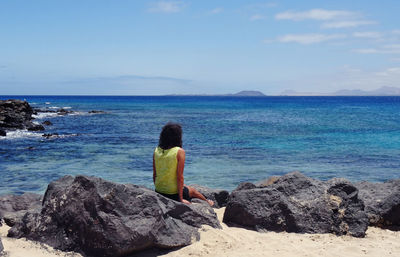 Scenic rear view of woman sitting on volcanic rock looking at atlantic ocean 