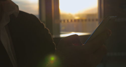 Close-up of man using mobile phone at sunset