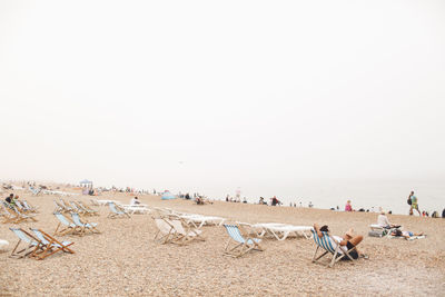 People relaxing at beach against sky during foggy feather