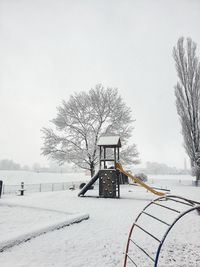 Bare tree on snow covered field against sky