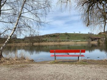 Empty bench by lake against sky