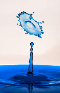 Close-up of drop splashing on water against blue background