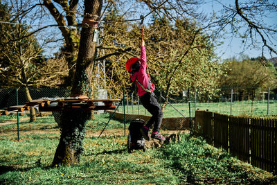 Little girl with protections practicing climbing between trees with ropes and nets