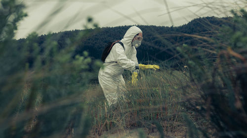 Side view of woman in protective workwear standing by plants