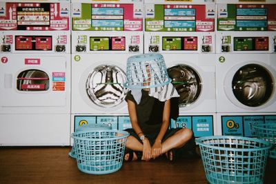 Young woman wearing laundry basket in laundromat