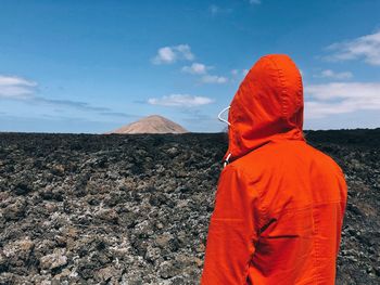 Rear view of person in red hooded shirt on landscape against sky