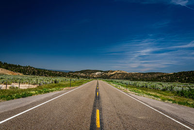 Empty road amidst green landscape against blue sky