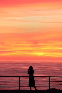 Silhouette woman looking at sea against orange sky