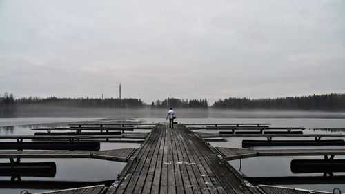 Rear view of man on pier at lake against sky