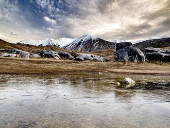 Lake by rocks and mountains against sky