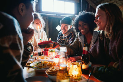 Male and female friends talking while enjoying food on table in log cabin