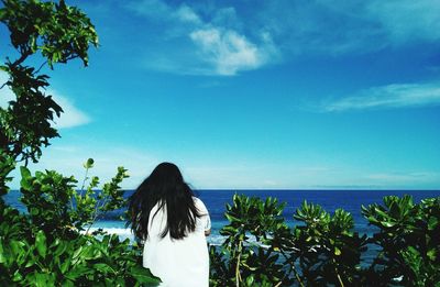 Rear view of woman standing by sea against blue sky