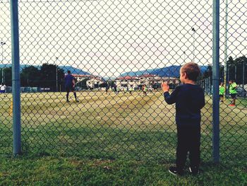 Man standing on field seen through chainlink fence