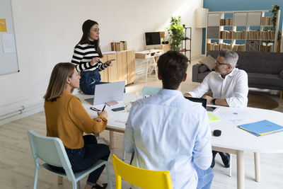 Young businesswoman discussing with colleagues sitting on desk at office