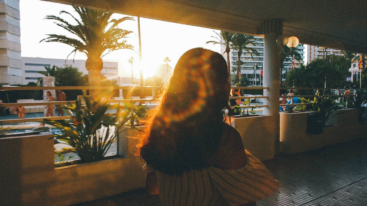 REAR VIEW OF WOMAN LOOKING THROUGH WINDOW AT BUILDING