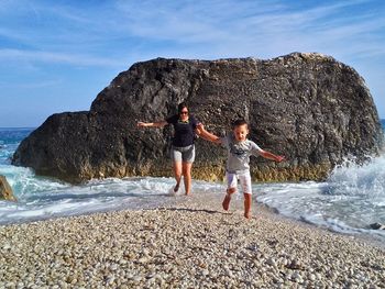 Mother and son running on shore against rock formation at beach