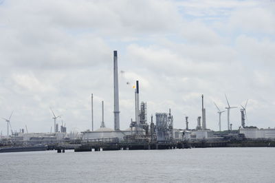 View of factory by sea against sky