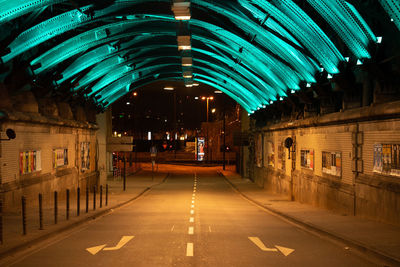 Empty road along illuminated buildings at night