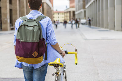 Back view of young man with backpack pushing his bike