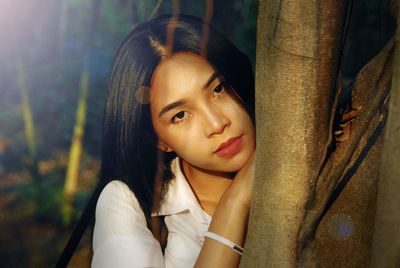 Portrait of young woman leaning on tree at forest