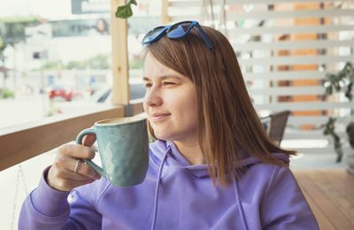 Young pretty woman in purple hoodie  drinking enjoying cappuccino coffee or tea on the cafe terrace