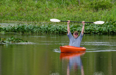  senior male happily raises his oar over his head in triumph as he sits in his kayak