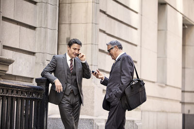 Businessmen using mobile phones while standing at city street